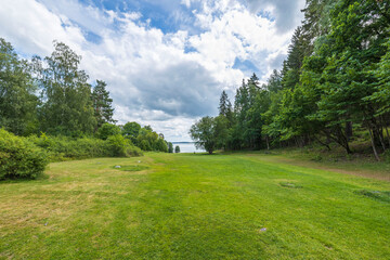 Beautiful summer nature landscape view. Greengrass field on front and Baltic sea on cloudy sky background.