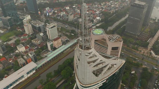 Aerial pedestal tilting into overhead view of the top of the Wisma 46 skyscraper in Jakarta, Indonesia on a cloudy day
