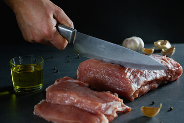 Cooking. Male hands with a knife cut a large piece of raw fresh meat on a stone gray background next to spices