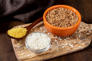 Rice, buckwheat, and millet in bowls on a brown wooden table. Gluten-free cereals