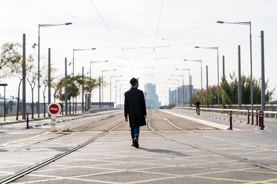 Fashionable young man walking between railroad tack on city street