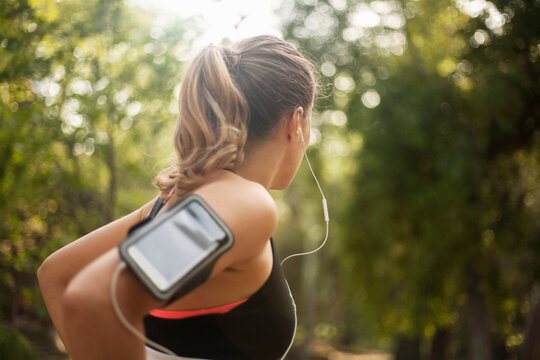 Young sportswoman with in-ear headphones listening music while standing outdoors