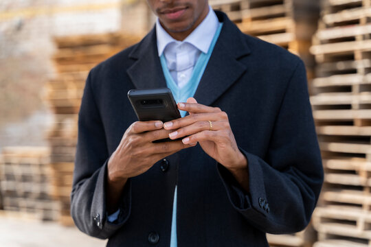 Young man using mobile phone against pallets