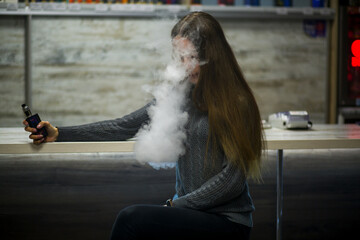 Vaping teenager. Young pretty white caucasian teenage girl with long hair smoking an electronic...