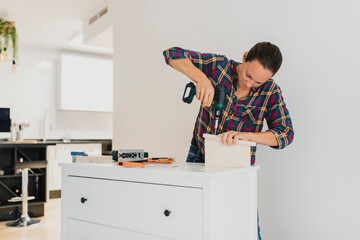 Craftsperson using electric screwdriver while standing by cabinet at home