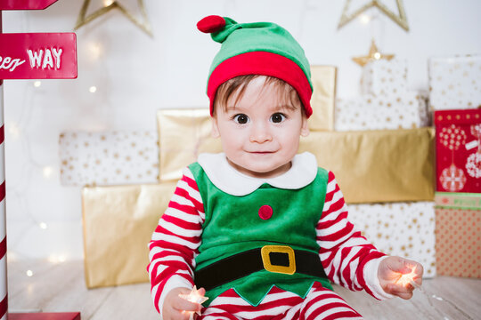 Cute baby boy in elf costume playing while sitting at home during Christmas