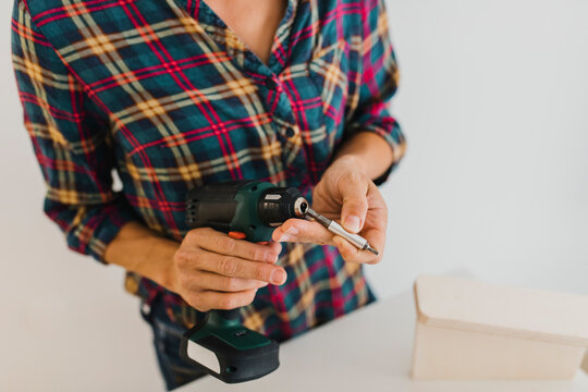 Woman putting screwdriver bit in power tool while standing at home