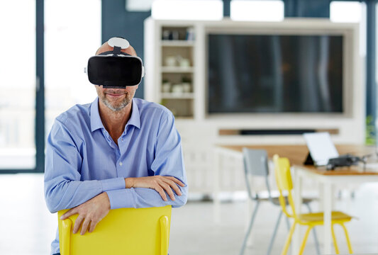 Smiling businessman using virtual reality headset while leaning on chair at home