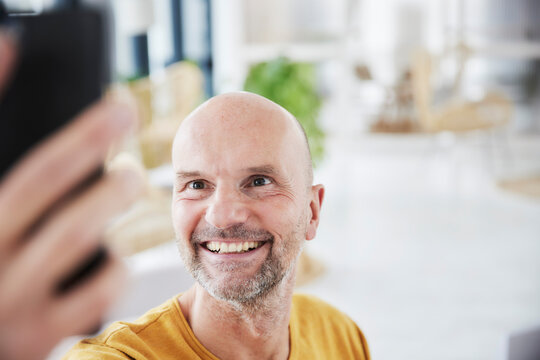 Mature man taking selfie through smart phone while standing at home
