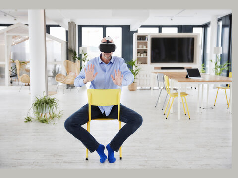 Mature businessman using virtual reality headset while sitting on chair at home office