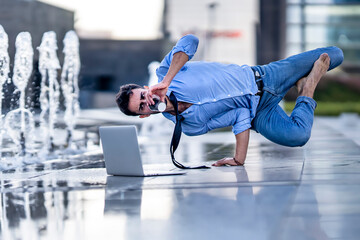 Young businessman with laptop drinking coffee while doing handstand by fountain on footpath