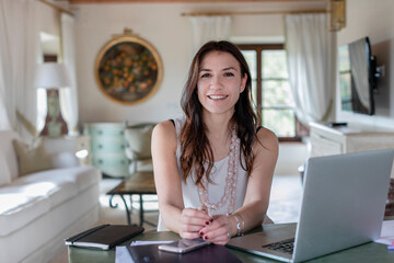 Smiling female event planner sitting by laptop at home