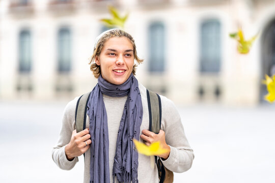 Smiling man with shawl and backpack looking away while standing in city during autumn