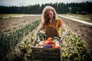 Smiling farm worker carrying vegetable box while standing at farm