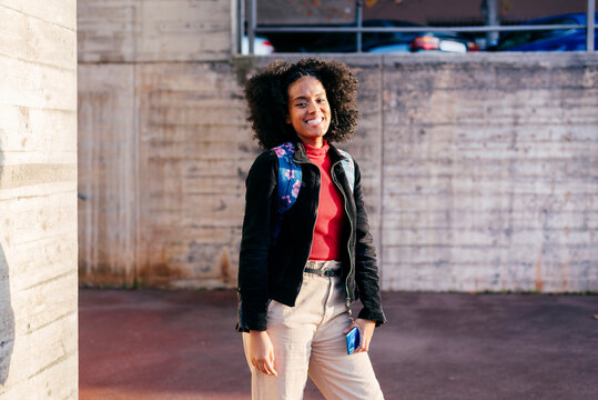 Female student with backpack smiling while standing against wall