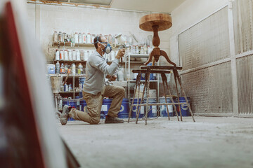 Craftsperson wearing protective face mask spraying on table while standing at workshop