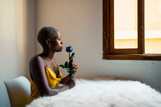 Thoughtful woman sitting with blue rose at white fur table