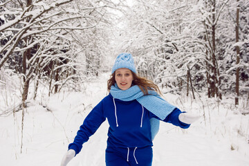 Fototapeta na wymiar woman in a blue tracksuit white mittens and scarf stands in winter in a snow covered forest
