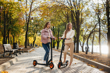 Two young beautiful girls ride electric scooters in the Park on a warm autumn day