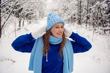 woman in a blue tracksuit white mittens and scarf stands in winter in a snow covered forest