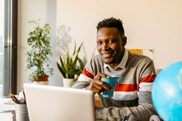 Smiling male entrepreneur sitting with coffee cup in home office