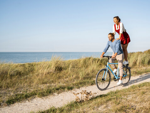 Young woman enjoying ride with man while standing on bicycle against clear sky