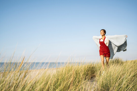 Smiling woman covered in shawl running with arms outstretched against clear sky