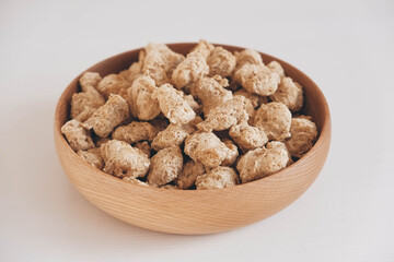 Raw dehydrated soy meat or dry soya chunks in wooden plate on white background. Copy, empty space for text