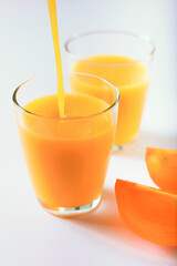Pouring healthy persimon juice into glasses on white
