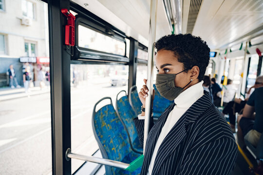 Young businesswoman looking through window while traveling in bus during COVID-19