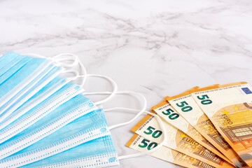 Medical masks and euro bills on a marble background, the concept of expenditure on masks that have been made in the context of the global COVID-19 pandemic and the fight against the coronavirus.