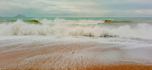 Storm waves in a rough sea on a pebble beach with the Peñon de Ifach in the background