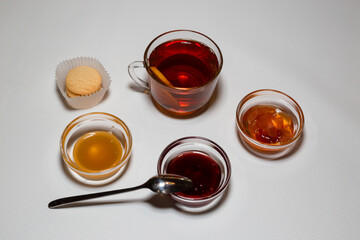 A cup of strong tea, rosettes with raspberry jam, apples and honey. White background.