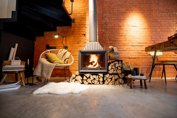Cozy fireplace with firewood in the loft style home interior with brick wall background, burning fire in the fireplace, house coziness in winter - obrazy, fototapety, plakaty