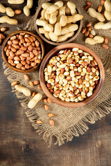 Roasted, raw peanuts and shelled in wooden bowls on a brown wooden table. The view from the top	