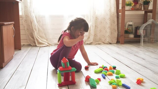 Little beautiful girl sits on the floor in the room and plays with a colorful constructor