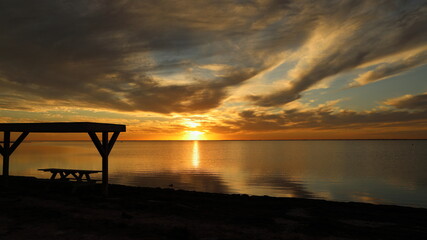 Silhouetted picnic table on the beach during a gorgeous sunset from Padre Island, Texas; clouds and sun reflected in water; copy space
