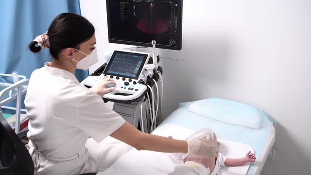 Ultrasound examination of a newborn baby. Woman doctor in mask and gloves diagnoses a child in a modern clinic with modern equipment1