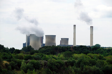 Fototapeta na wymiar Cooling towers and chimneys with steam clouds of a power plant in a woodland - Stockphoto