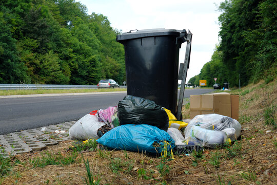 Graue M&uuml;lltonne und Illegale M&uuml;llentsorgung auf Parkplatz neben Bundesstra&szlig;e - Stockfoto