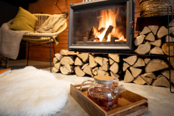Cozy place by the fireplace with firewood, hot drink and sheepskin in a beautiful loft-style interior