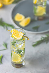 Refreshing lemon lime drink with ice cubes in glass goblets against a light gray background. Summer fresh lemon soda cocktail with rosemary, selective focus