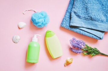 Obraz na płótnie Canvas Green liquid soap package, shampoo bottle, blue sponge, towel and lavender flowers on a pink background. Flat lay still life beauty photography