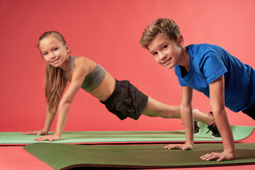 Cheerful kids doing plank exercise against red background