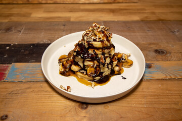 A delicious plate of Banoffee Pecan and Chocolate Pancakes draped in Chocolate and toffee source, on a wooden kitchen table