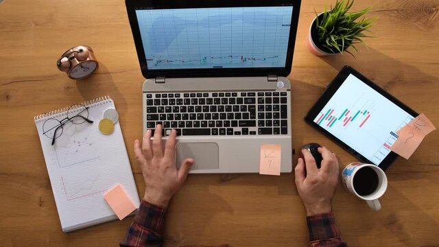 Man working from home with a leptop is holding the graphical screen with the mouse.