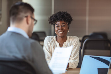 Portrait of joyful  woman smiling and holding resume while sitting in front of businessman during...