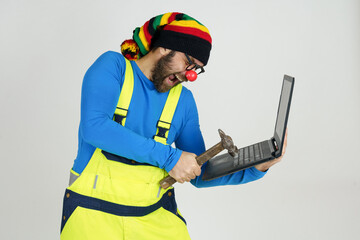 A clown in a bright suit holds a laptop in his hands, hits it with a hammer