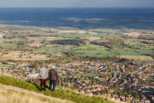 Walking companions take in the view of Great Malvern town set amongst the English countryside from the top of the Malvern hills, Worcestershire, England