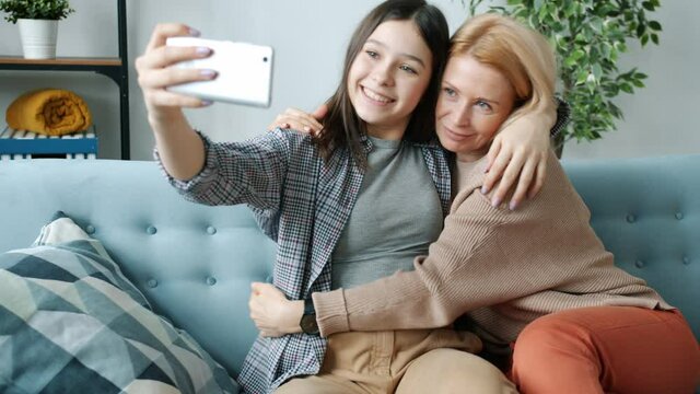 Teenager pretty girl is taking selfie with mature mom hugging woman making funny faces laughing at home. Family lifestyle and leisure time activities concept.